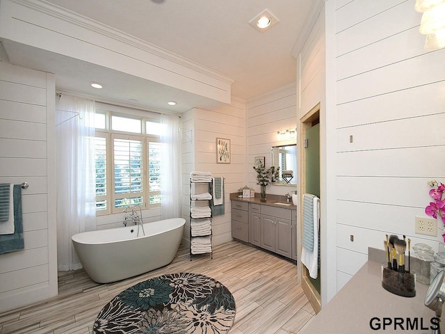 bathroom featuring vanity, wooden walls, crown molding, and a tub