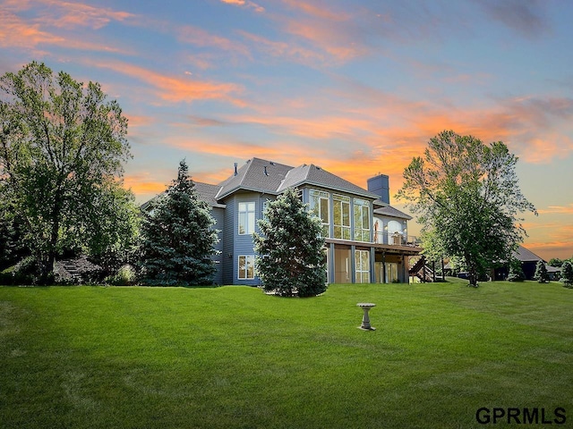 back house at dusk featuring a yard and a wooden deck