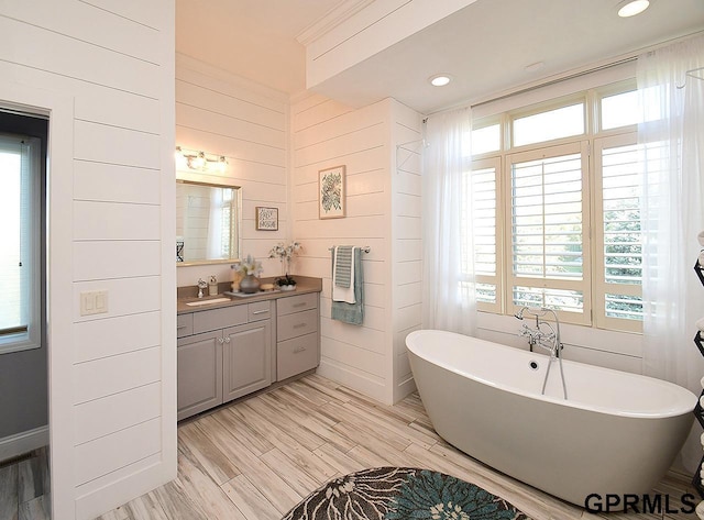 bathroom with vanity, wood walls, a healthy amount of sunlight, and a bath