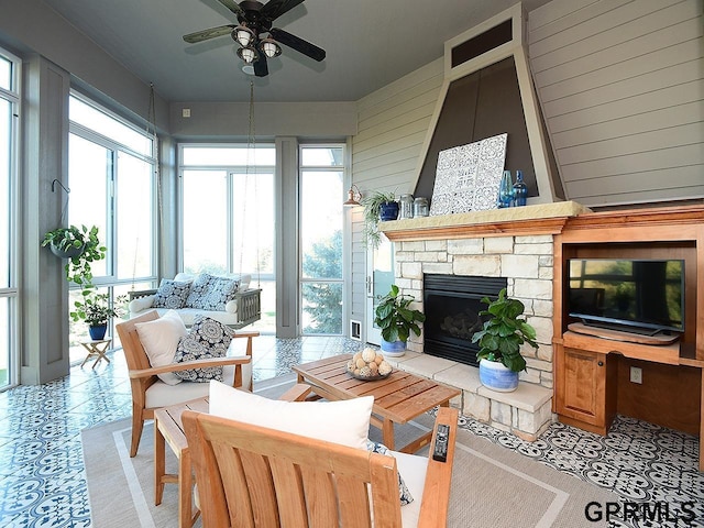 sunroom / solarium with a stone fireplace and ceiling fan