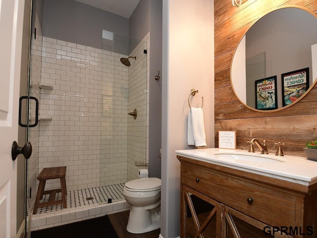 bathroom with vanity, toilet, a shower with door, and wooden walls