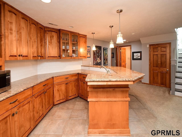 kitchen with light stone countertops, kitchen peninsula, tasteful backsplash, light tile patterned floors, and hanging light fixtures