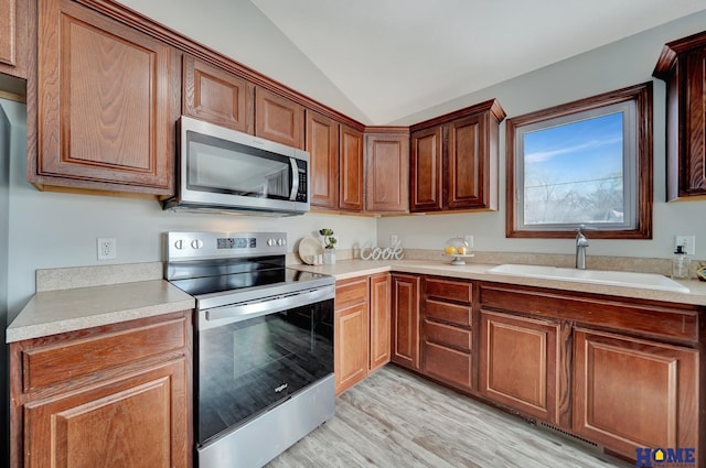 kitchen featuring appliances with stainless steel finishes, light hardwood / wood-style flooring, lofted ceiling, and sink