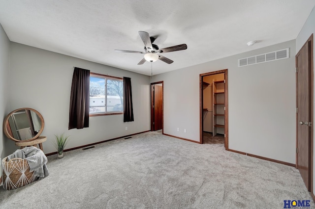 unfurnished bedroom featuring a walk in closet, a closet, ceiling fan, and light colored carpet