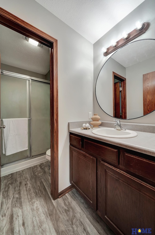 bathroom with a textured ceiling, hardwood / wood-style floors, toilet, walk in shower, and vanity