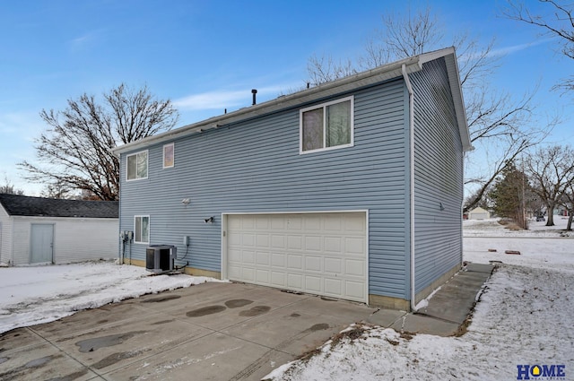 snow covered back of property with central air condition unit and a garage