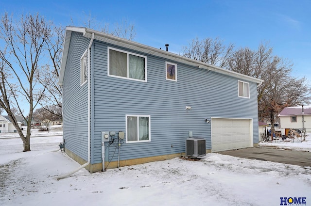 snow covered house featuring a garage and cooling unit