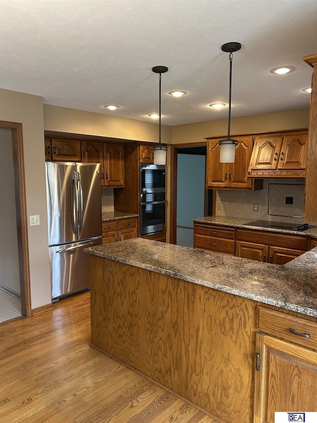 kitchen featuring appliances with stainless steel finishes, light wood-type flooring, tasteful backsplash, dark stone counters, and hanging light fixtures