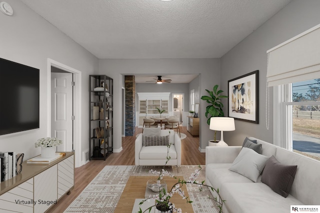 living room with light wood-type flooring, a textured ceiling, and ceiling fan