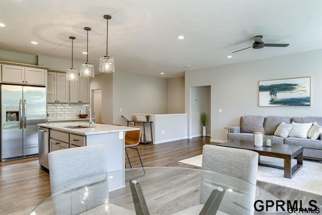 interior space with sink, hanging light fixtures, light stone counters, an island with sink, and appliances with stainless steel finishes