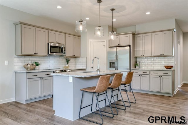 kitchen with sink, backsplash, pendant lighting, a center island with sink, and appliances with stainless steel finishes