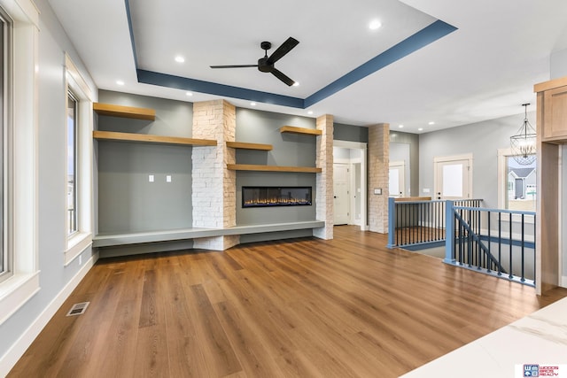 unfurnished living room with ceiling fan with notable chandelier, a large fireplace, a raised ceiling, and hardwood / wood-style floors