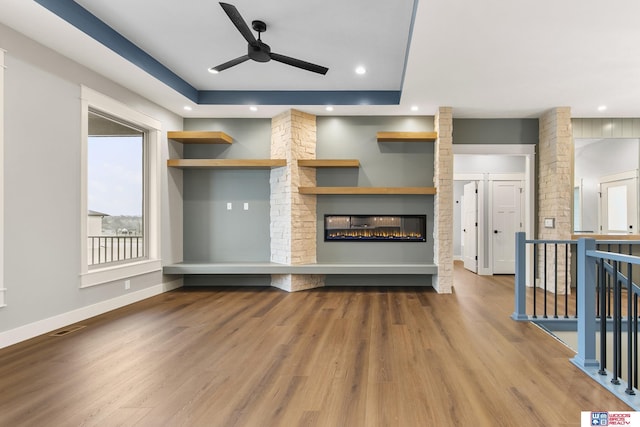 unfurnished living room featuring ornate columns, wood-type flooring, a raised ceiling, and ceiling fan