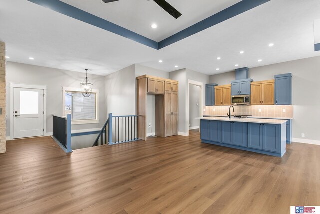 kitchen featuring sink, tasteful backsplash, hanging light fixtures, light hardwood / wood-style flooring, and an island with sink