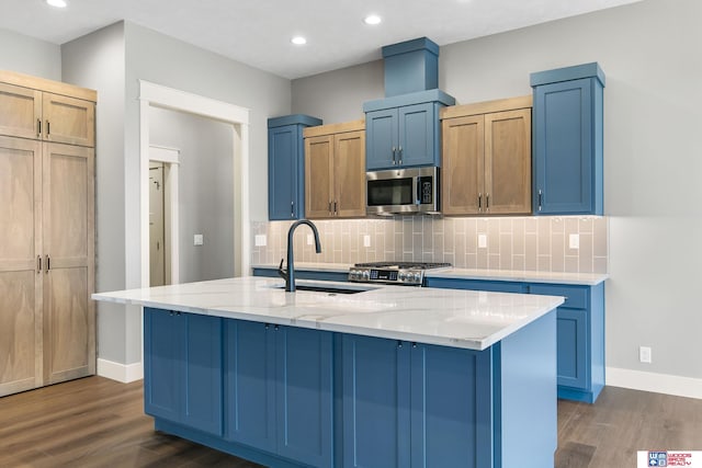 kitchen featuring an island with sink, sink, stainless steel appliances, light stone countertops, and dark wood-type flooring