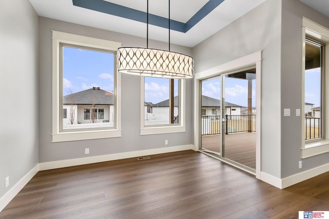 unfurnished dining area featuring dark hardwood / wood-style floors and a tray ceiling