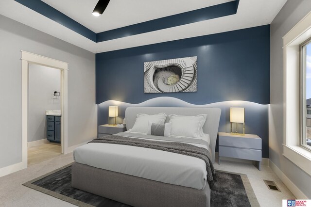 bedroom featuring ensuite bathroom, a tray ceiling, and light carpet