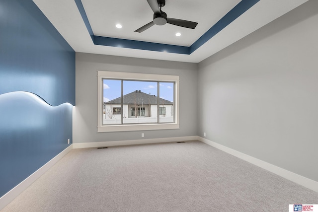 unfurnished room with a raised ceiling, carpet, and ceiling fan