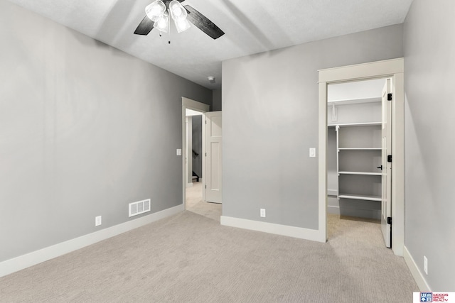 unfurnished bedroom featuring light carpet, a spacious closet, a closet, and ceiling fan