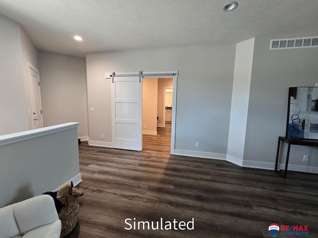 spare room with a textured ceiling, a barn door, and dark wood-type flooring