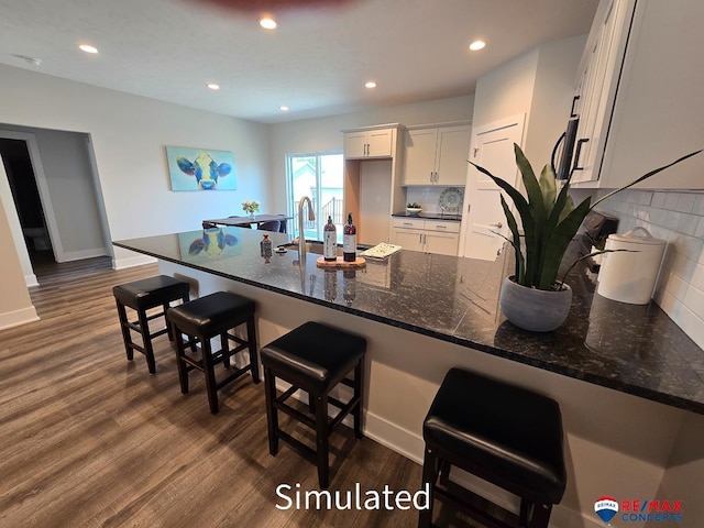 kitchen with dark wood-type flooring, tasteful backsplash, dark stone counters, a kitchen bar, and white cabinets