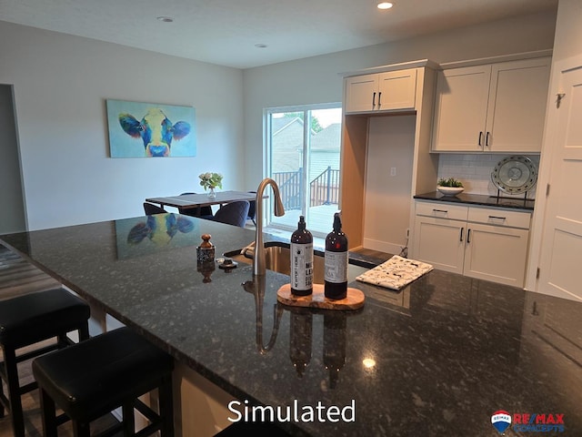 kitchen featuring decorative backsplash, a kitchen bar, white cabinetry, and dark stone counters