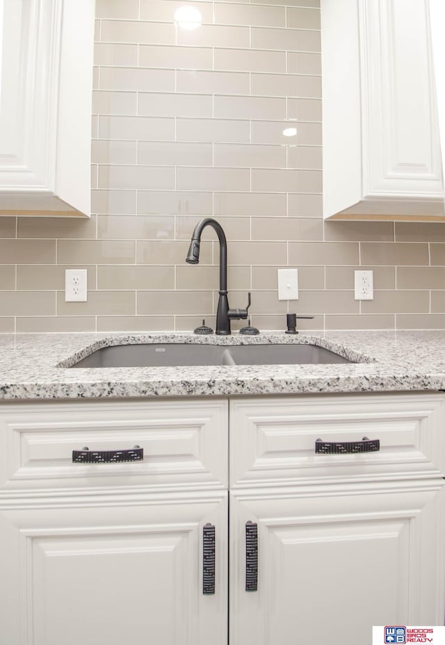 interior details featuring backsplash, light stone countertops, sink, and white cabinets