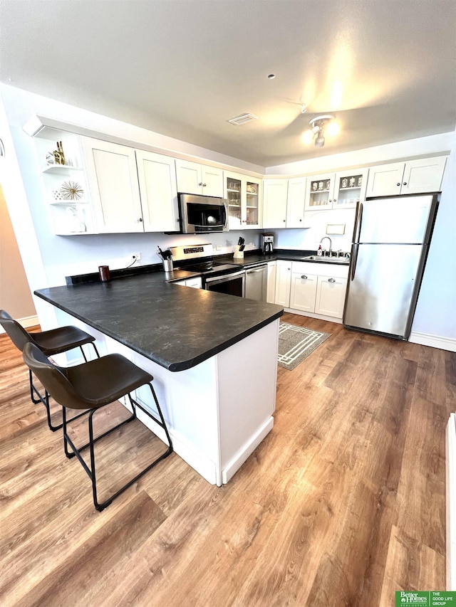 kitchen with kitchen peninsula, white cabinets, light hardwood / wood-style floors, and appliances with stainless steel finishes