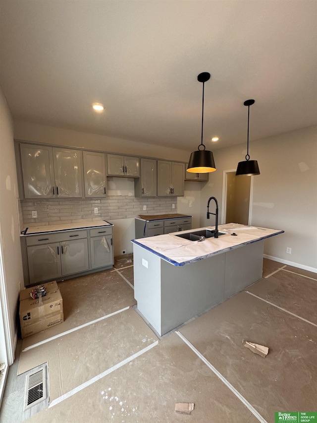 kitchen with a kitchen island with sink, gray cabinetry, hanging light fixtures, decorative backsplash, and sink