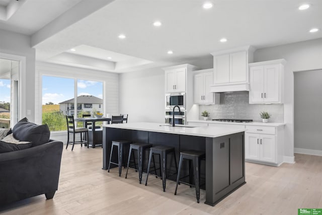 kitchen featuring stainless steel microwave, white cabinetry, sink, and an island with sink