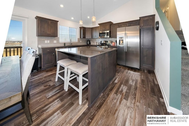 kitchen featuring sink, stainless steel appliances, vaulted ceiling, decorative light fixtures, and a kitchen island