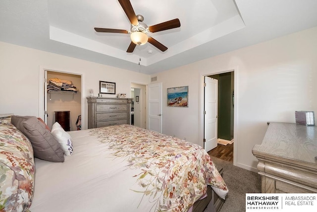 carpeted bedroom featuring ceiling fan, a raised ceiling, a spacious closet, and a closet