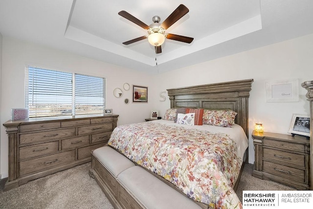 carpeted bedroom with ceiling fan and a raised ceiling