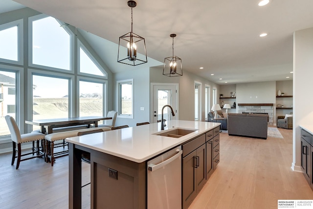 kitchen featuring pendant lighting, dishwasher, a stone fireplace, an island with sink, and sink