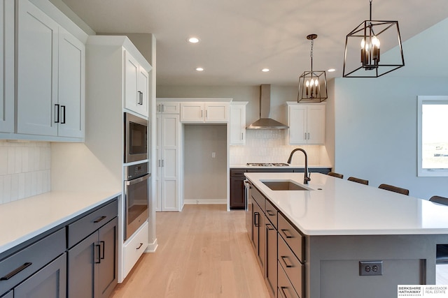 kitchen featuring appliances with stainless steel finishes, wall chimney exhaust hood, hanging light fixtures, and a kitchen island with sink