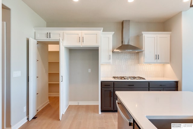 kitchen featuring white cabinetry, stainless steel appliances, backsplash, wall chimney exhaust hood, and light hardwood / wood-style flooring