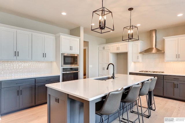 kitchen featuring stainless steel oven, wall chimney exhaust hood, white cabinetry, and a center island with sink