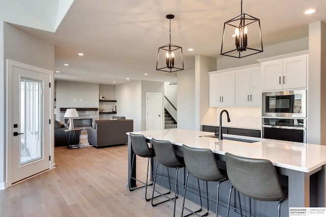 kitchen with a large island with sink, white cabinets, decorative light fixtures, sink, and oven