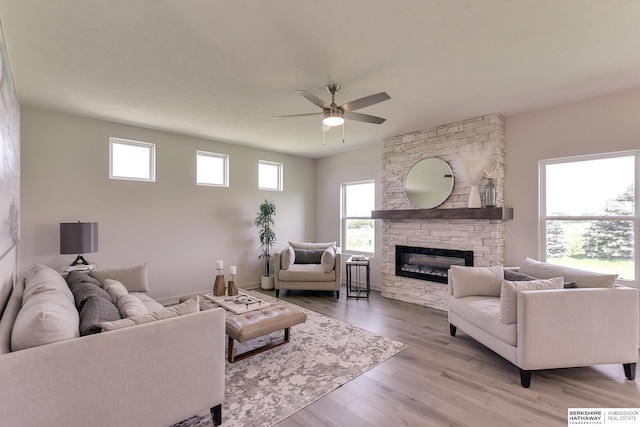 living room featuring light hardwood / wood-style flooring, ceiling fan, and a stone fireplace