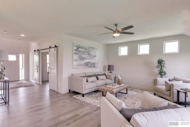 living room with light wood-type flooring, a barn door, ceiling fan, and a healthy amount of sunlight