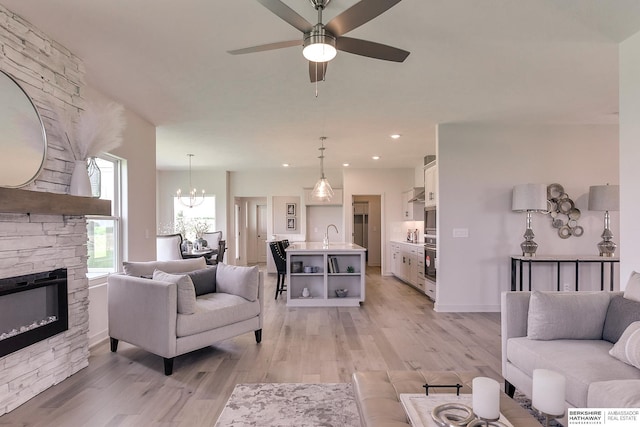 living room with sink, a fireplace, ceiling fan with notable chandelier, and light hardwood / wood-style flooring