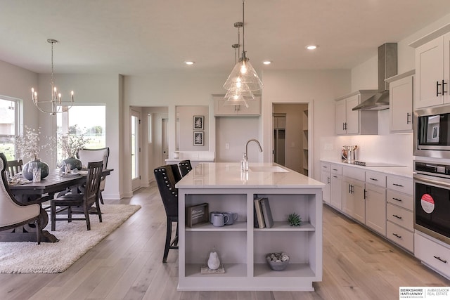 kitchen featuring a kitchen island with sink, hanging light fixtures, stainless steel appliances, and wall chimney range hood