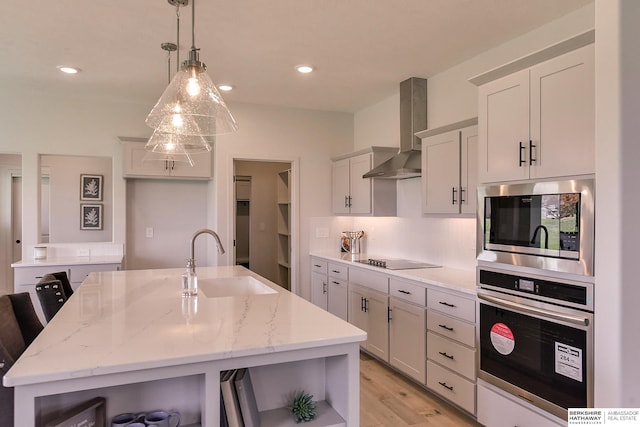 kitchen featuring sink, wall chimney exhaust hood, stainless steel appliances, an island with sink, and decorative light fixtures