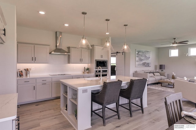 kitchen with ceiling fan, wall chimney exhaust hood, a barn door, pendant lighting, and appliances with stainless steel finishes