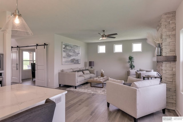 living room featuring ceiling fan, a barn door, and light wood-type flooring