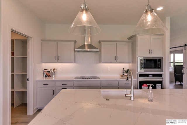 kitchen with a barn door, light stone counters, decorative light fixtures, and appliances with stainless steel finishes