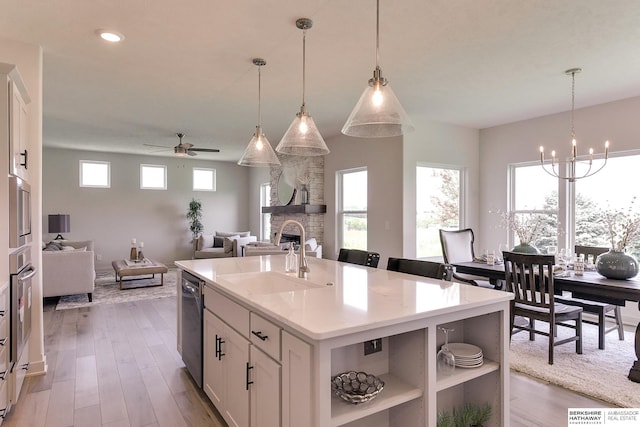 kitchen featuring pendant lighting, a center island with sink, white cabinets, sink, and a fireplace