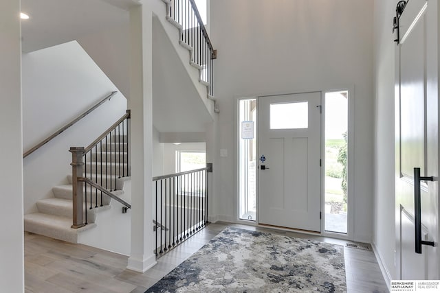 entryway with a barn door, light wood-type flooring, and a towering ceiling