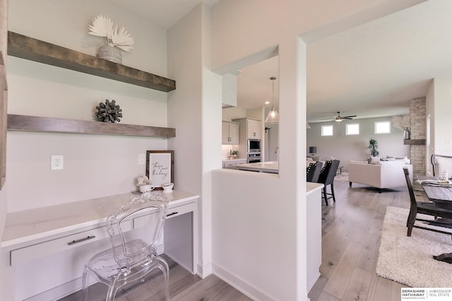 interior space with ceiling fan, pendant lighting, light hardwood / wood-style floors, white cabinetry, and stainless steel microwave