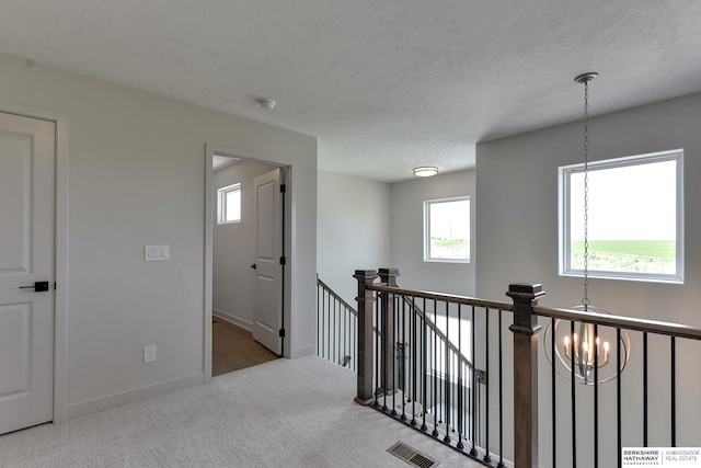 hallway with a textured ceiling, carpet floors, and an inviting chandelier